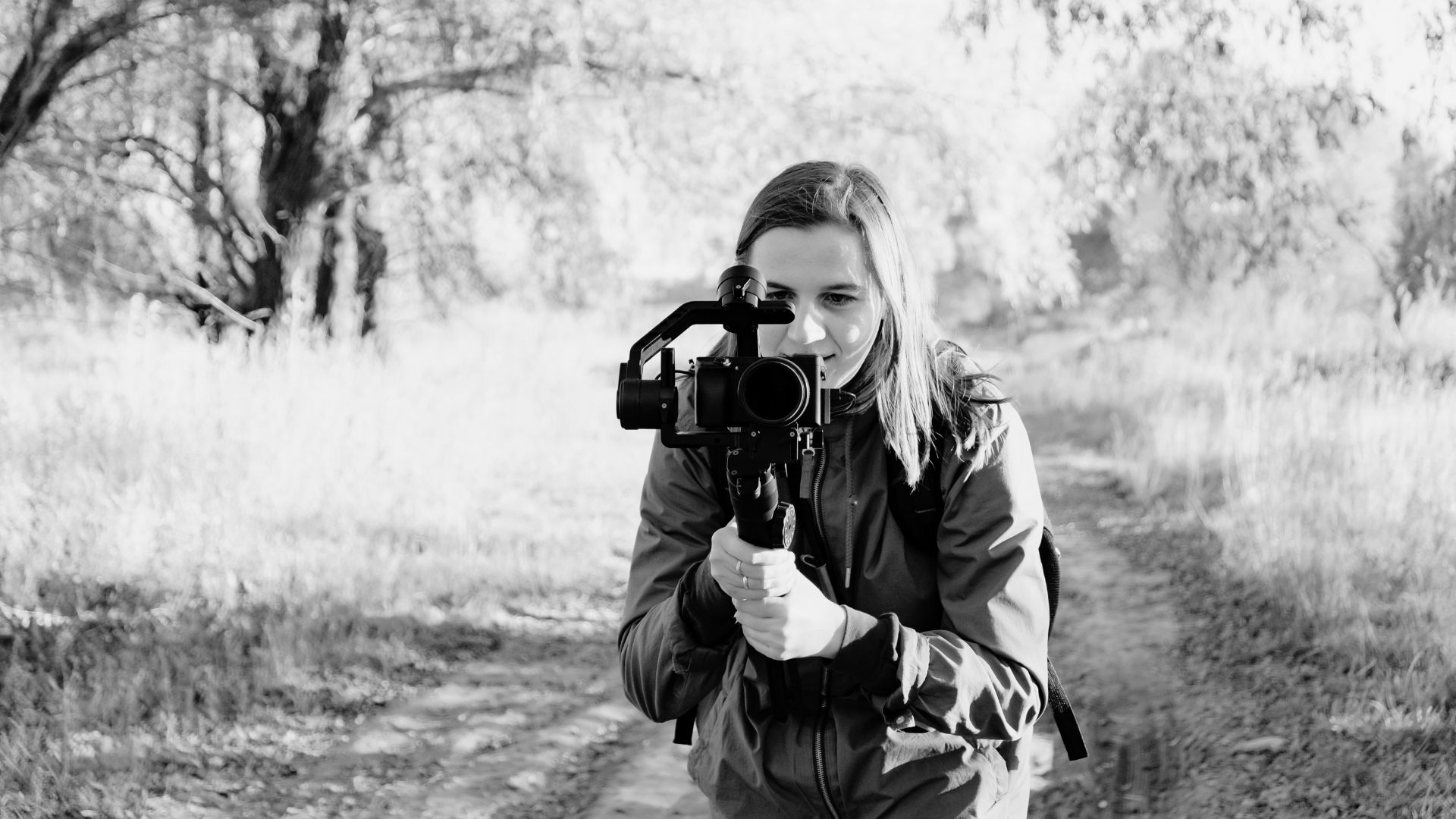 Black and white image of woman in nature setting pointing camera at viewer