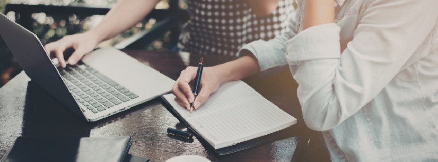 Two sets of hands writing. One on a laptop and the other in a notebook.