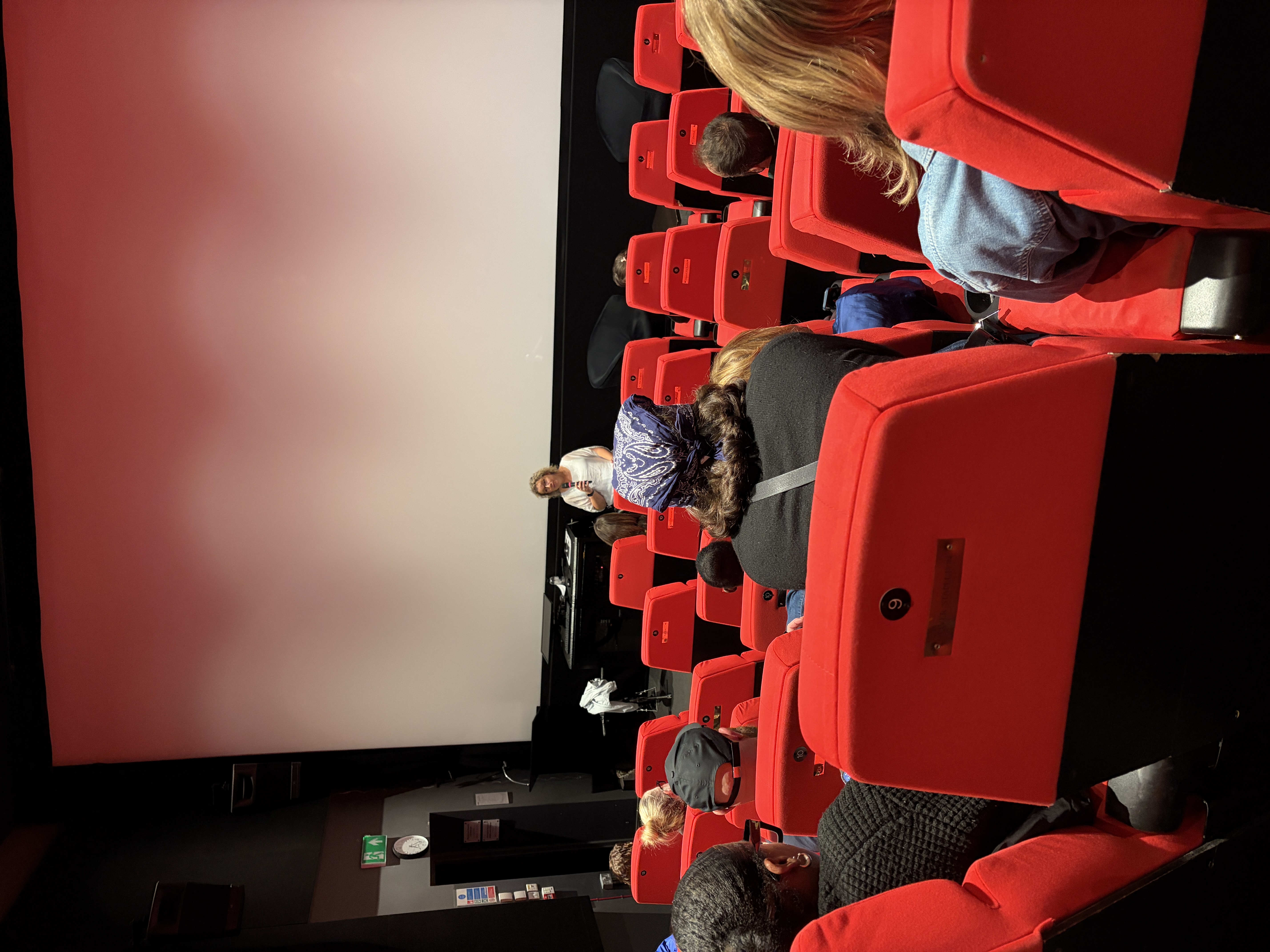 cinema full of people with person at front holding microphone
