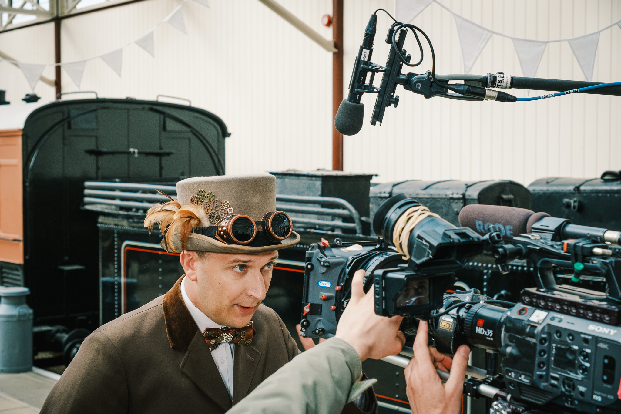 man wearing top hat and steampunk style costume with camera and boom mic in frame