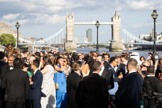 Sun setting on crowd gathered outside old billingsgate with the Thames and Tower Bridge in the background