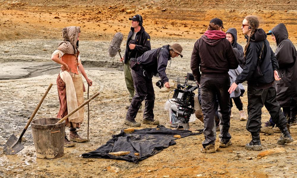 bts from student film showing woman in medieval period costume standing on clay beach with film crew around