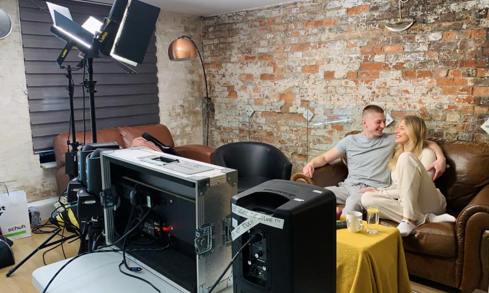two people sat on sofa in front of filming equipment