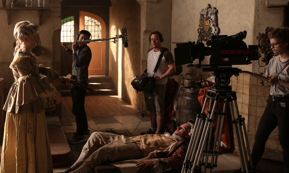 two actors in period clothing surrounded by production crew including location sound recordist