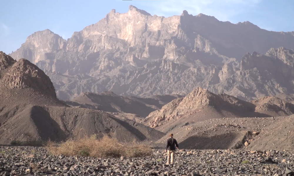 still from film showing man walking towards volcano in distance