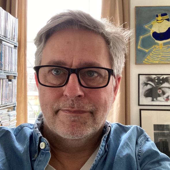 Man with grey hair and glasses sits in front of bookcase