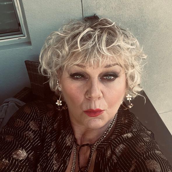 Colour image of woman with curly blonde hair and red lipstick looking at camera