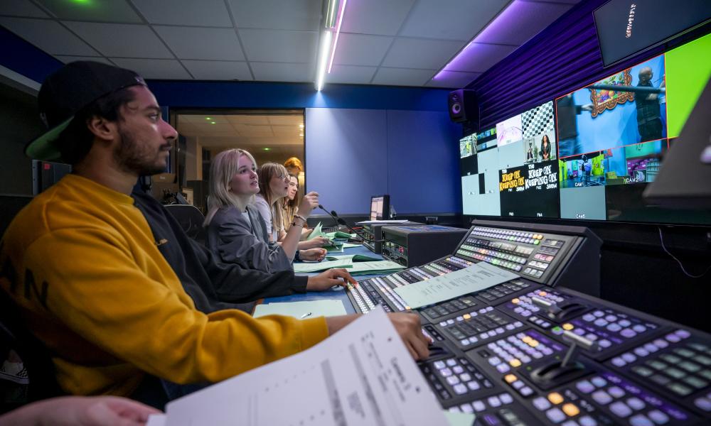 Students in the control room at the TV Studio, using the console to direct cameras, lights, cast, and crew 