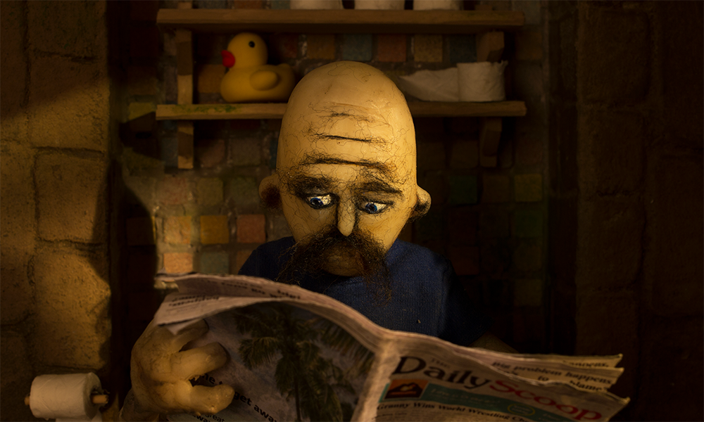 still from zuman showing man sitting on toilet reading newspaper